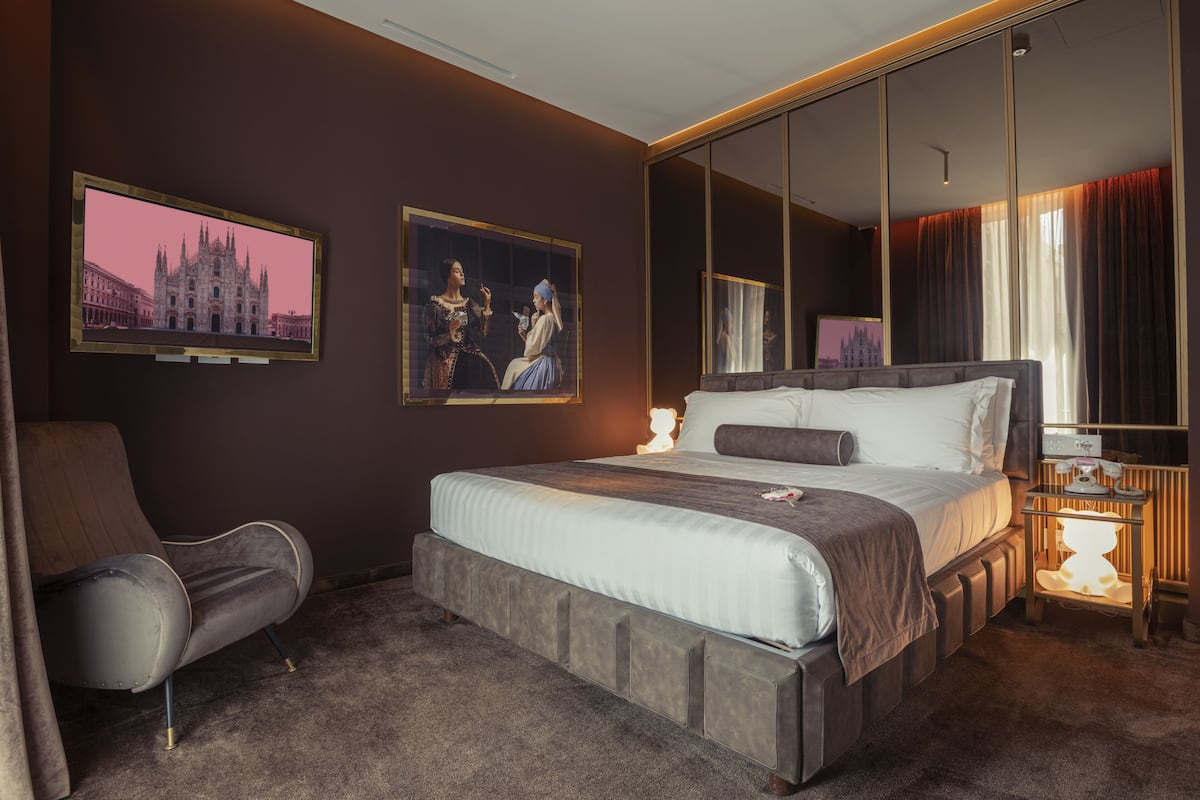 A modern hotel room with a large bed, a seating area, and artwork on the walls.