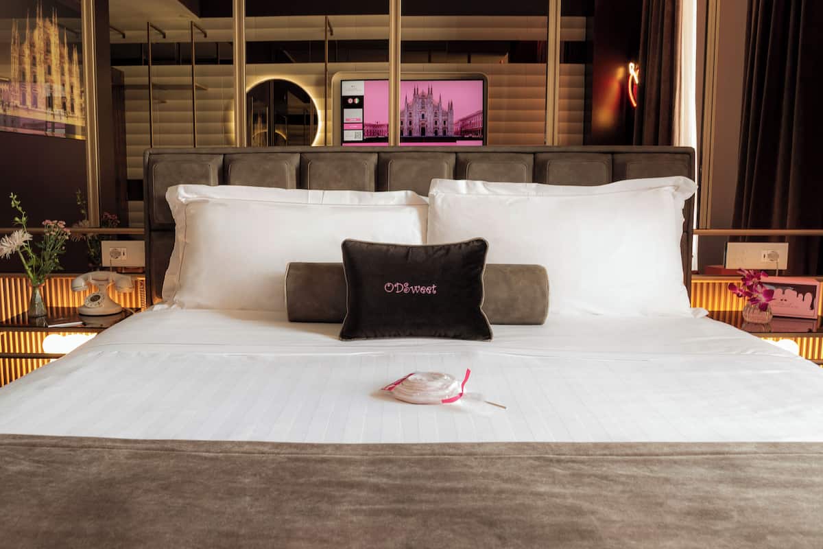 A hotel room with a large bed, a television mounted on the wall, and a decorative pillow.
