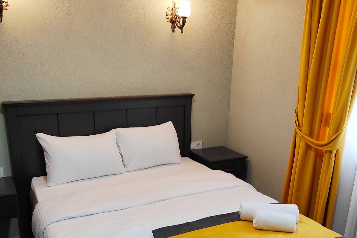 A neatly made bed with white and yellow bedding, a dark headboard, and two bedside tables.