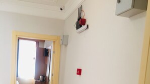 A hallway with wooden flooring, a door leading to a room, and a small shelf with a red object on the wall. - Lebon Hotel Old City (Istanbul)