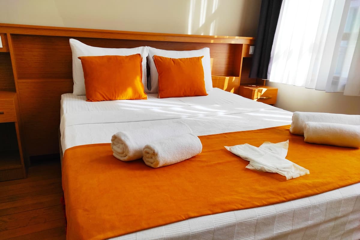 A neatly made bed with white and orange bedding, a wooden headboard, and a small bedside table.