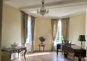 Una habitación con un piano, una mesa con un florero y una araña.