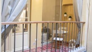 Ein Balkon mit Metallgeländer, einem kleinen Tisch, Stühlen und hängenden Pflanzkästen.