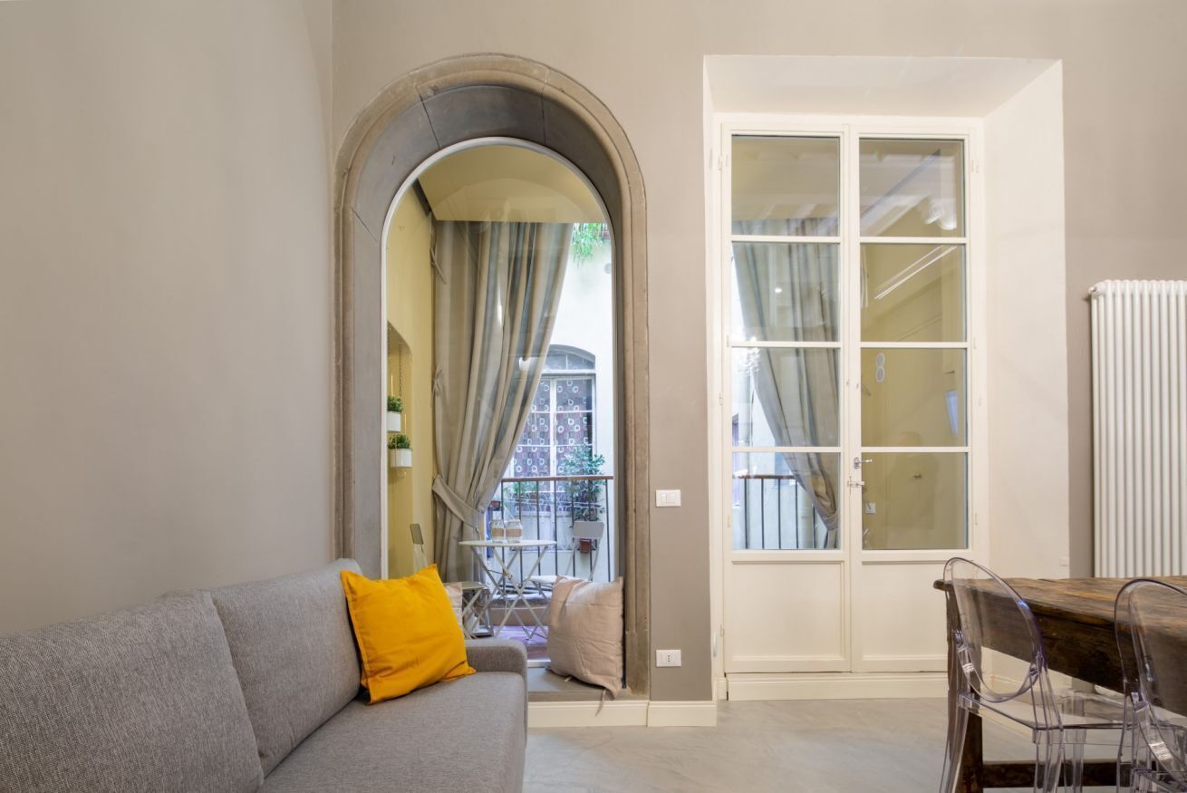 Ein Wohnzimmer mit grauem Sofa, einem Holztisch und einer Glastür, die auf einen Balkon führt.