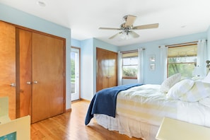 Ein Schlafzimmer mit Bett, Holzschrank, Deckenventilator und großen Fenstern.