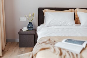 En pænt redt seng med hvide og beige puder, et natbord med en blomstervase og en bog på sengen.