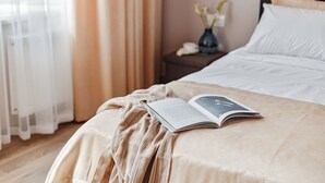 Un lit bien fait, avec un livre et une couverture à rayures, un vase rempli de fleurs et une table de chevet avec une lampe.