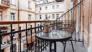 Un balcon avec une table ronde et des chaises en osier, un pot de fleurs et une balustrade en fer forgé.