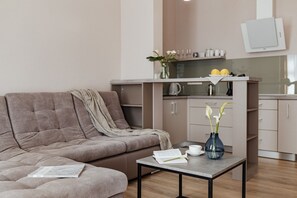En moderne stue med en sofa, et sofabord med en bog og en vase, samt et køkkenområde med skabe og en mikrobølgeovn.