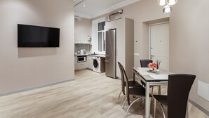 Une cuisine moderne dotée d’un téléviseur à écran plat, d’appareils électroménagers en acier inoxydable et d’un coin repas avec une table et des chaises.