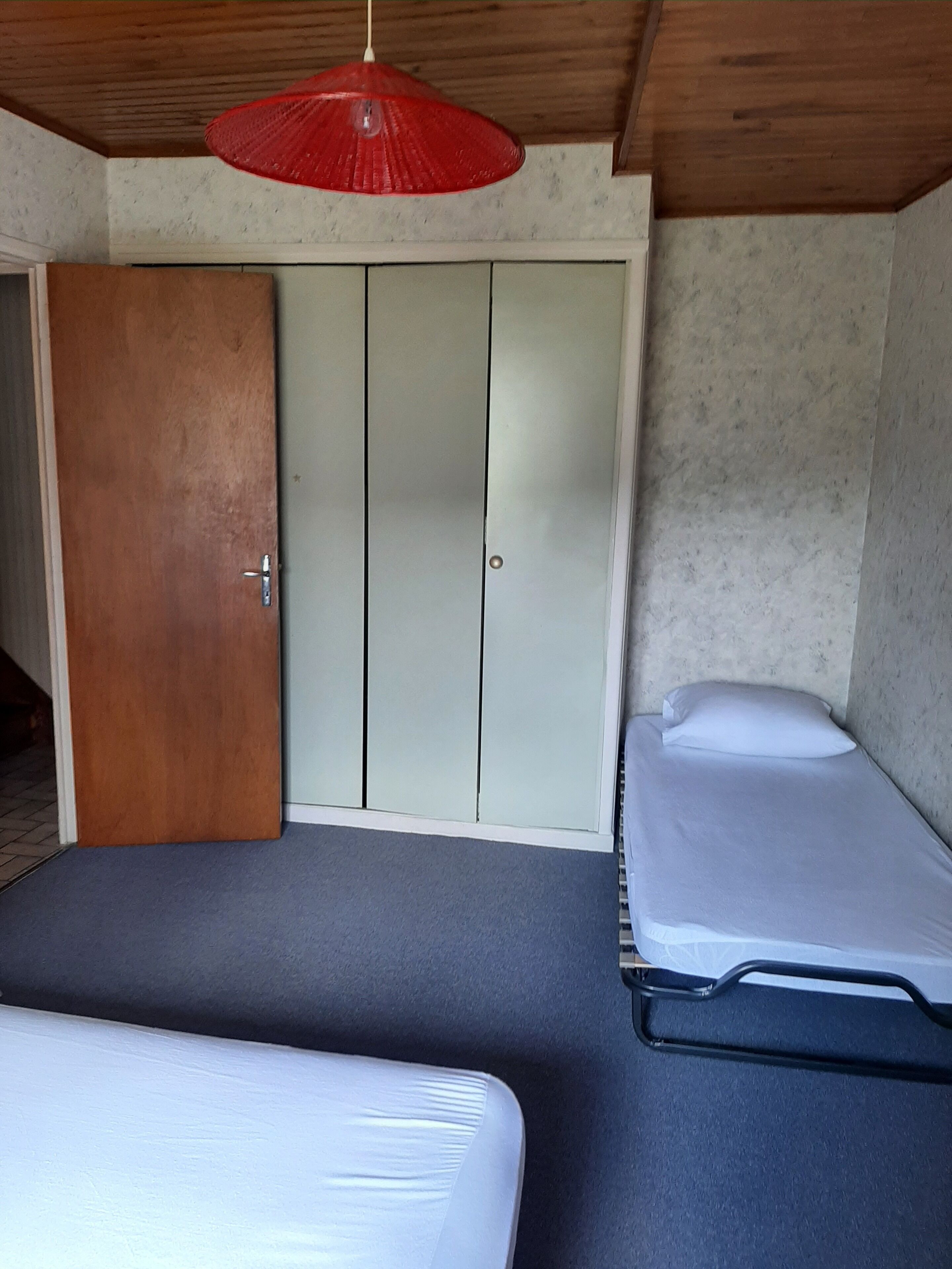 A room with two beds, a wardrobe, and a red hanging light fixture.