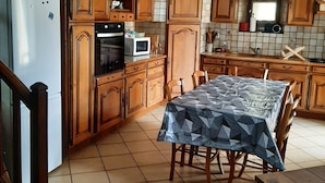 A kitchen with wooden cabinets, a dining table, a refrigerator, and a microwave. - Family house in the center of Lozère (BALSIEGES)