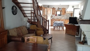 A cozy living room with a wooden dining table, sofa, and a staircase leading to a kitchen area. - Family house in the center of Lozère (BALSIEGES)