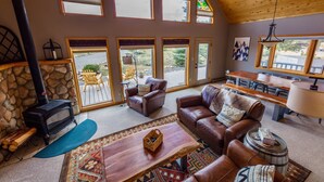 A cozy living room with a stone fireplace, leather sofas, a wooden coffee table, and large windows offering a view of the outdoors. - Ideal Mountain Retreat!   Peak Views, 15 Minutes to Salida and BV.   Fast WIFI. (Nathrop)
