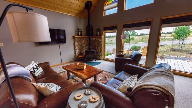 A cozy living room with leather sofas, a stone fireplace, and a large window offering a view of the outdoors. - Ideal Mountain Retreat!   Peak Views, 15 Minutes to Salida and BV.   Fast WIFI. (Nathrop)