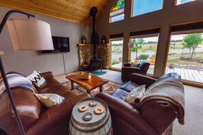 A cozy living room with leather sofas, a stone fireplace, and a large window offering a view of the outdoors. - Ideal Mountain Retreat!   Peak Views, 15 Minutes to Salida and BV.   Fast WIFI. (Nathrop)