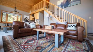 A spacious living area with a wooden staircase, leather sofas, a patterned rug, and a view of the outdoors. - Ideal Mountain Retreat!   Peak Views, 15 Minutes to Salida and BV.   Fast WIFI. (Nathrop)