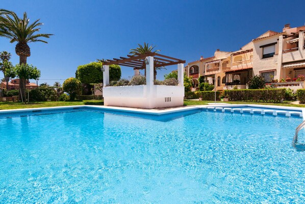 A swimming pool with a pergola, surrounded by well-maintained lawns and palm trees.