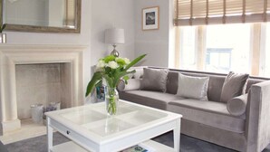 A living room with a fireplace, a sofa, a coffee table, and a vase of flowers. - Central Bath House Group Accommodation (Bath)