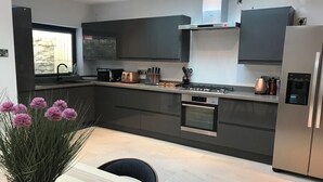 A modern kitchen with dark cabinetry, a gas stove, an oven, and a refrigerator. - Central Bath House Group Accommodation (Bath)