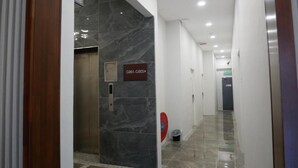Pasillo moderno de hotel con paredes de mármol, un ascensor y un cartel que indica las habitaciones G001-G005.