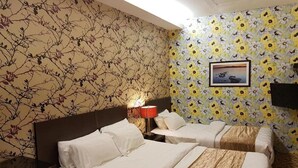 Una habitación de hotel con dos camas, una mesita de noche con lámpara y una pared con papel tapiz floral.