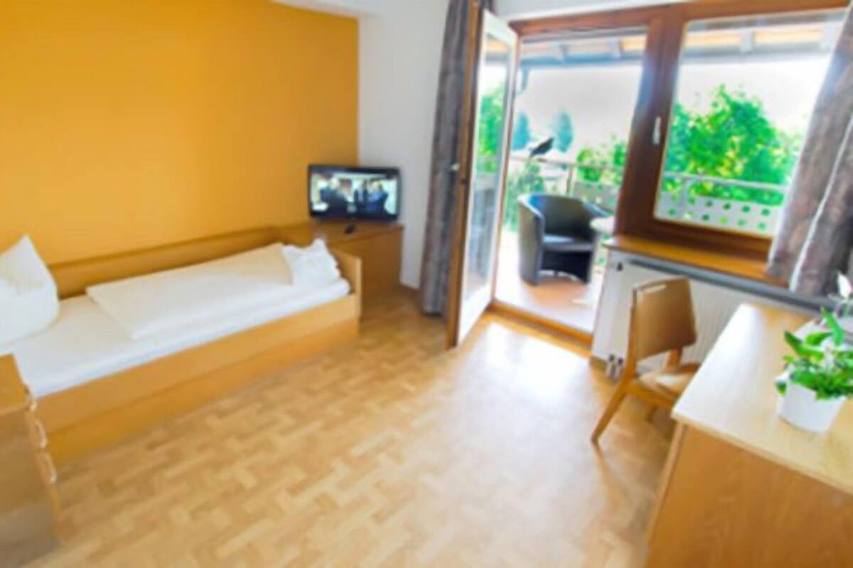 Une pièce dotée d’un plancher en bois, d’un canapé-lit, d’une télévision, d’un bureau avec une chaise et d’une fenêtre donnant sur un paysage verdoyant.