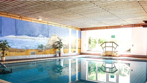 Ein Hallenbad mit Wandgemälde, Rettungsschwimmerstation und Topfpflanzen.
