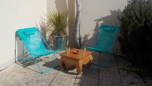 Two blue folding chairs, a wooden table with a bowl and a glass, and a potted plant against a wall. - Charming T2 house in a quiet condominium near the beaches. (Vaux-sur-Mer)