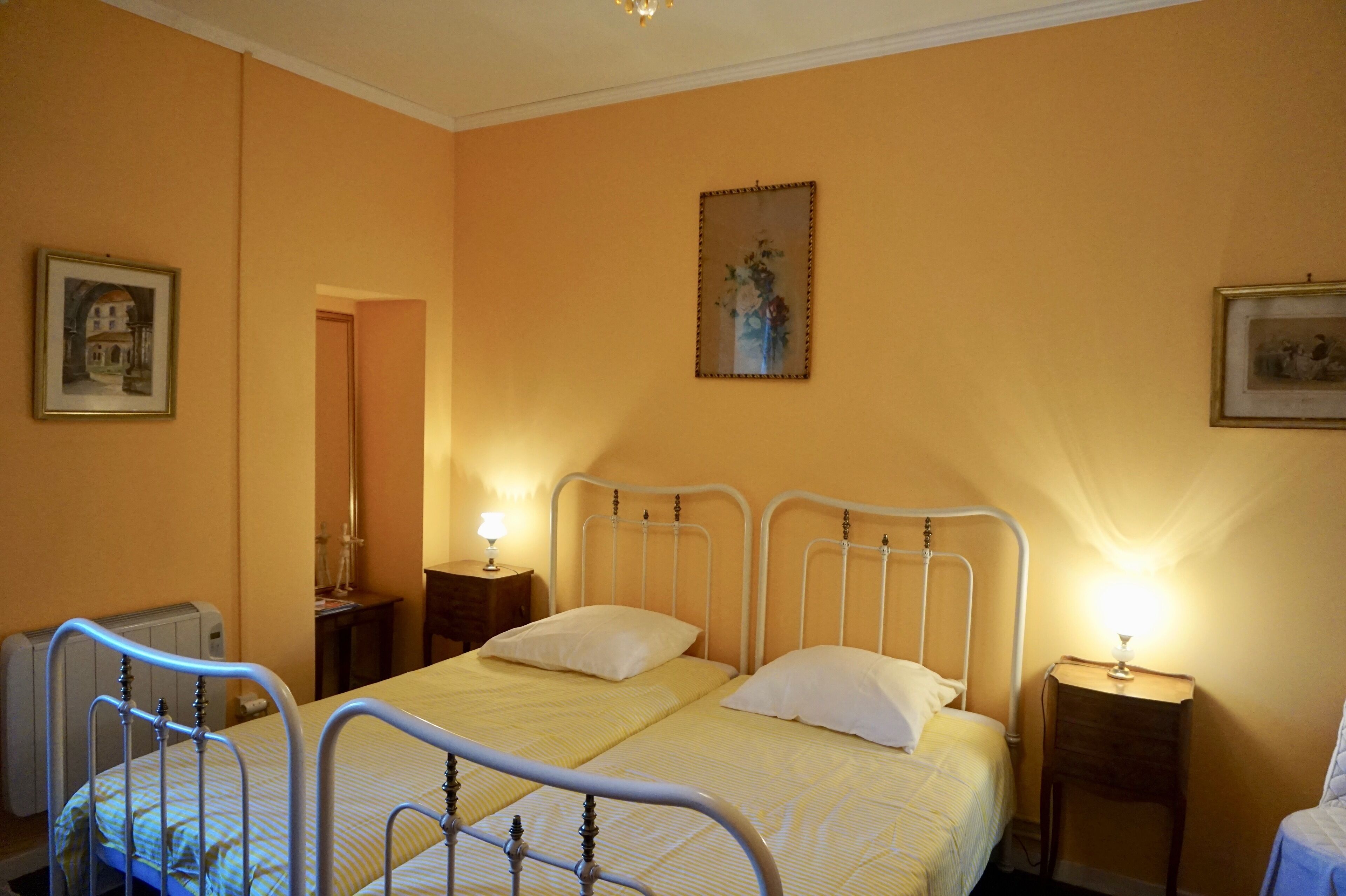 A bedroom with two beds, a radiator, a nightstand with a lamp, and a framed picture on the wall.