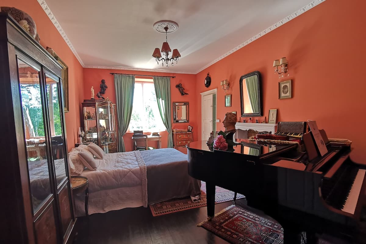 Un dormitorio con cama, piano, cómoda y ventana con cortinas.