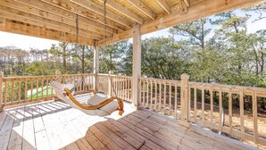 Un patio in legno con una poltrona a dondolo, ringhiere in legno e vista su alberi e vegetazione.