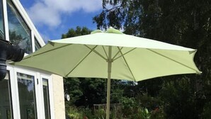 A patio with a table and chairs, a green umbrella, and a glass door leading to a garden. - Bron Hafren (Montgomery)