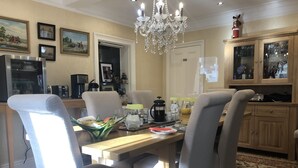 A dining area with a wooden table, four grey upholstered chairs, a chandelier, and a kitchen area with wooden cabinets and a refrigerator. - Bron Hafren (Montgomery)