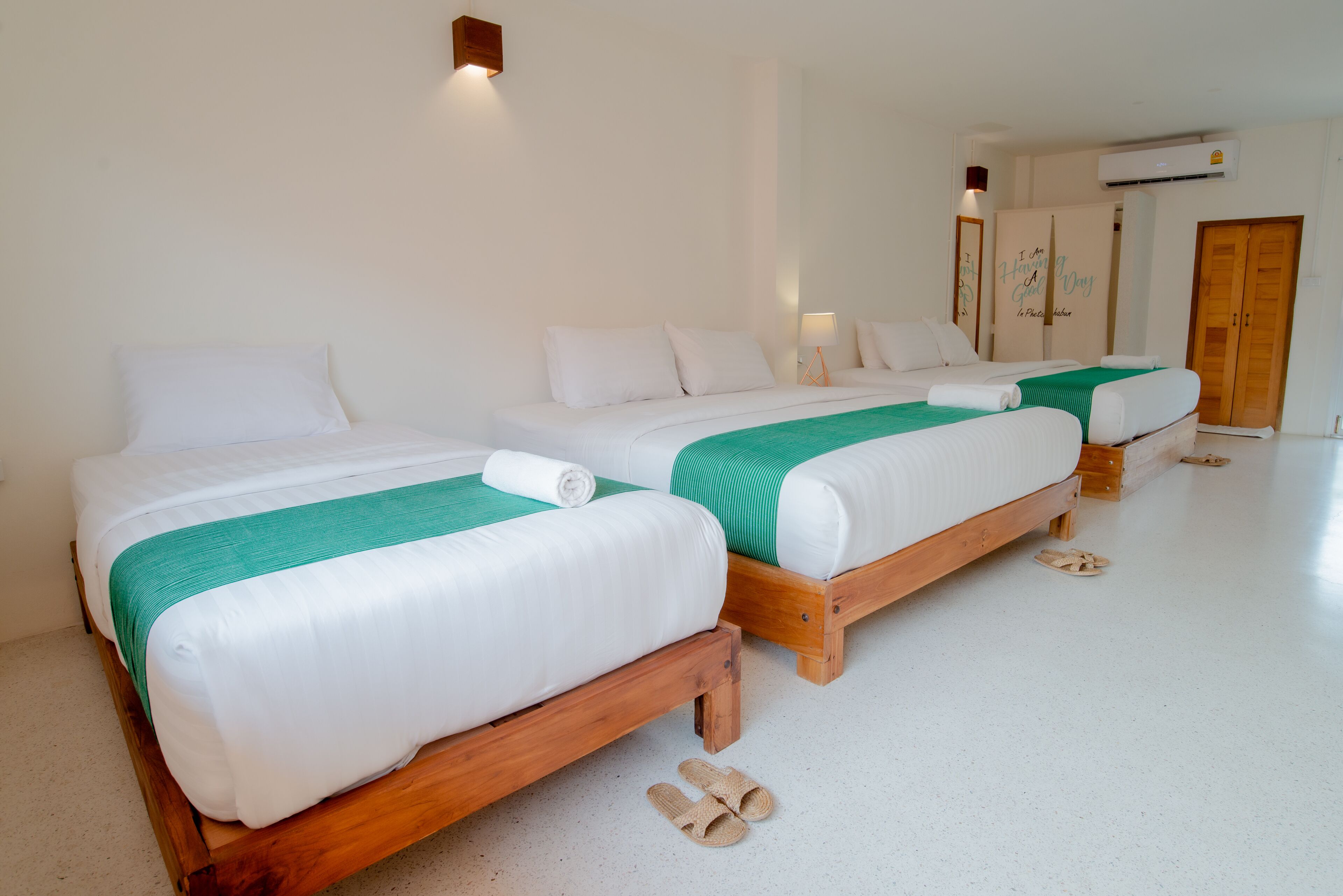 A hotel room with three wooden beds, each with white bedding and a green accent.