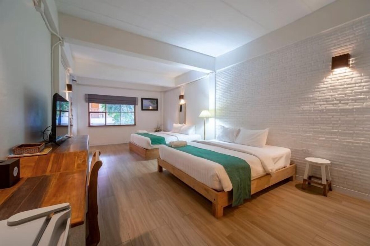 Une chambre d’hôtel avec deux lits, un bureau, une chaise, un petit tabouret et un téléviseur.