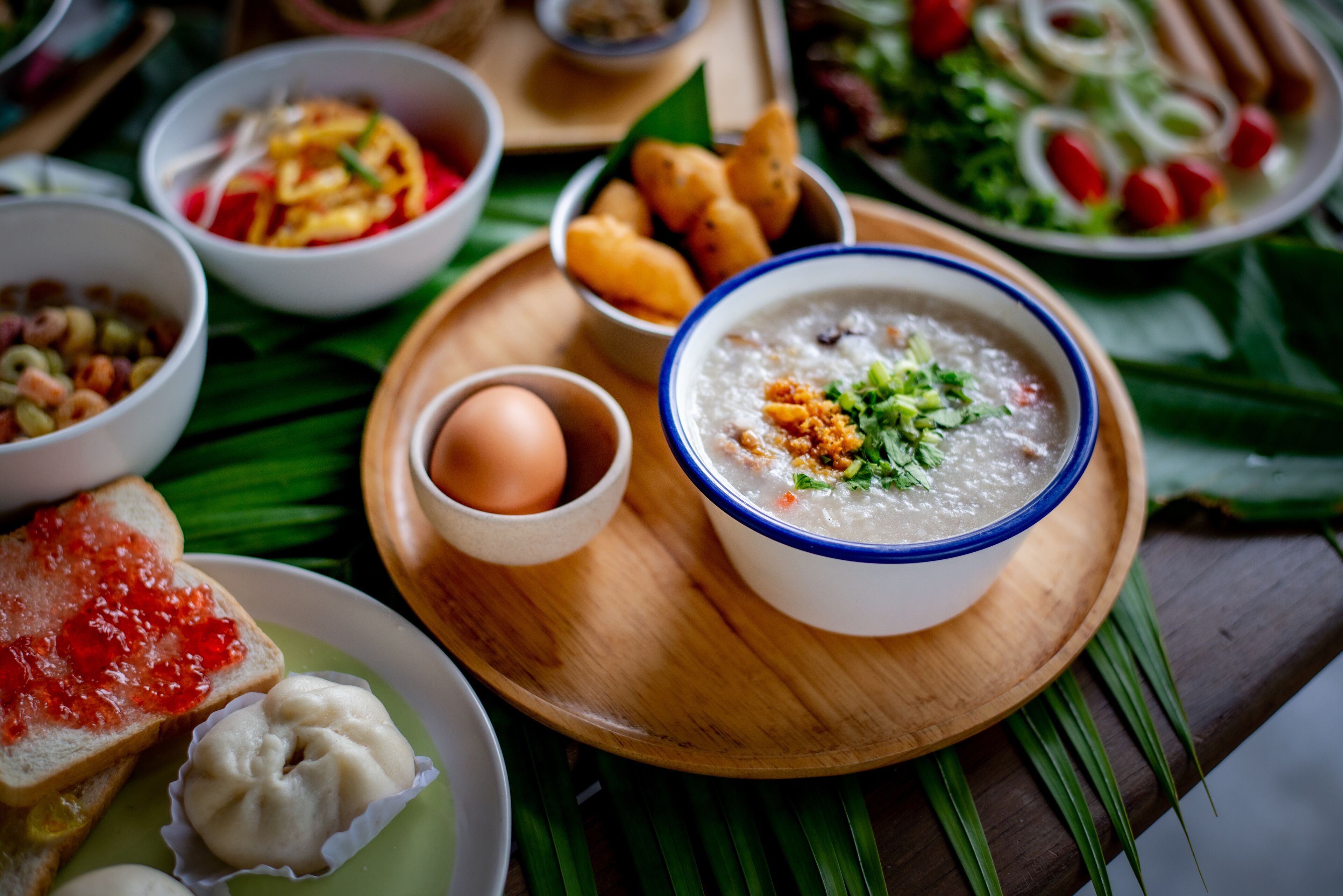 A variety of dishes including a bowl of congee, dumplings, and a plate of toast with jam.