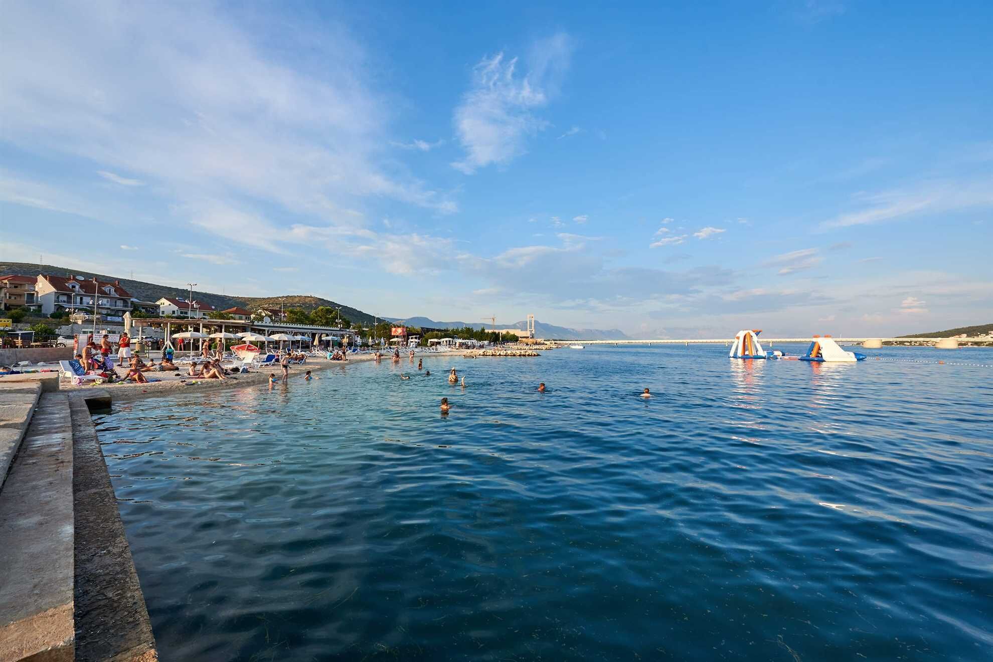A coastal beach scene with people swimming and sunbathing.