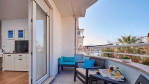 En balkon med siddeplads, spisebord og et køkken, der ses gennem en glasdør.