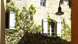 Un cortile con un edificio in pietra, un cancello in metallo e una campana.