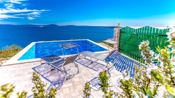 A swimming pool with lounge chairs, a stone wall, and a view of the sea. - Small robinson house with pool (Vinišce)