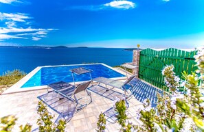 A swimming pool with lounge chairs, a stone wall, and a view of the sea.
