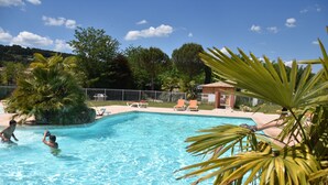 A swimming pool with clear blue water, surrounded by palm trees and lounge chairs. - Camping La Nouzarede (Joyeuse)