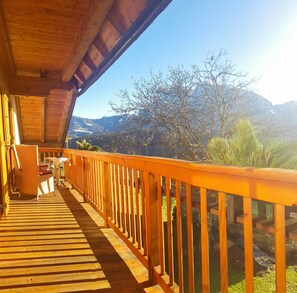 A wooden balcony with a view of mountains and a clear sky.