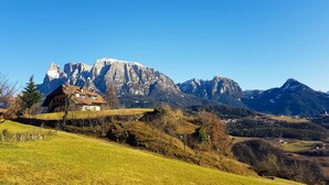 Um chalé tradicional com telhado inclinado, localizado numa encosta gramada com montanhas ao fundo.