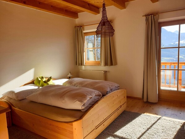 A wooden bed in a room with a window, curtains, and a hanging light fixture.