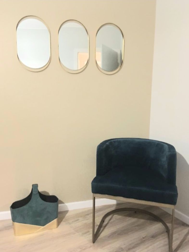 Une pièce comprenant un fauteuil recouvert d’un tissu turquoise, un petit panier turquoise et trois miroirs ovales accrochés au mur.