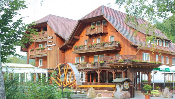 A wooden hotel with multiple balconies, a water wheel, and outdoor seating areas. - Untere Kapfenhardter Mühle (Schoemberg)