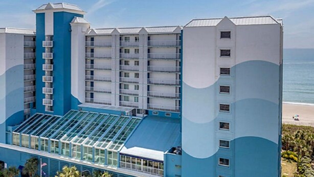 Een hotel met meerdere verdiepingen, in blauw-wit gebouwd, met balkons en een zwembad.