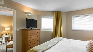 Hotelkamer met een bed, een televisie op een dressoir, een raam met jaloezieën en een lamp op een nachtkastje.